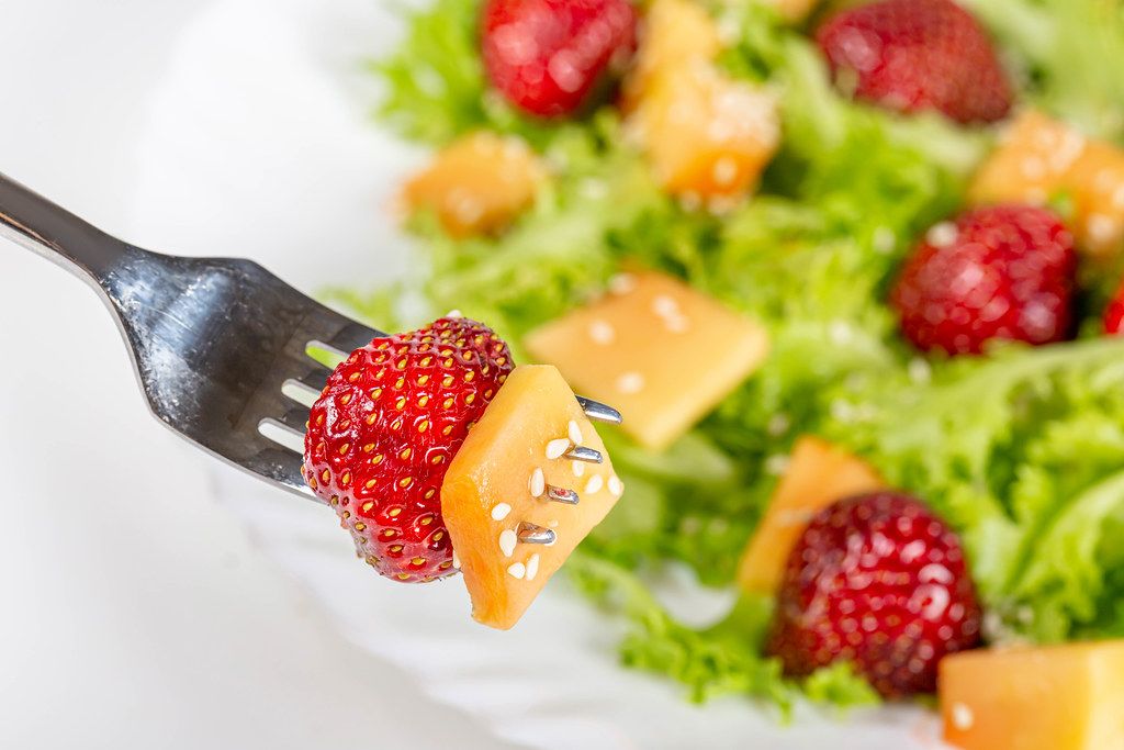 Close-up, mango and strawberry slices on a fork with sesame seeds