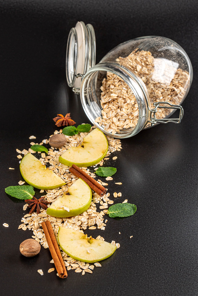 Close-up, oatmeal with apples, cinnamon, anise, nutmeg and mint scattered on a black background with a glass jar