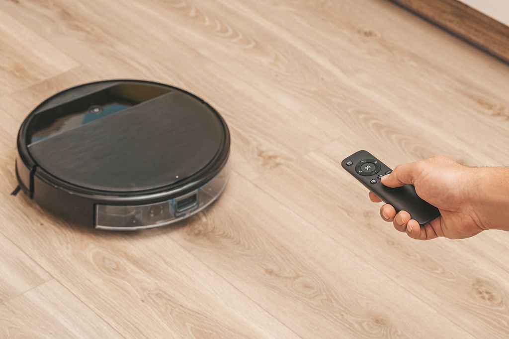 Close-up of a man holding remote control of robotic vacuum cleaner to start cleaning