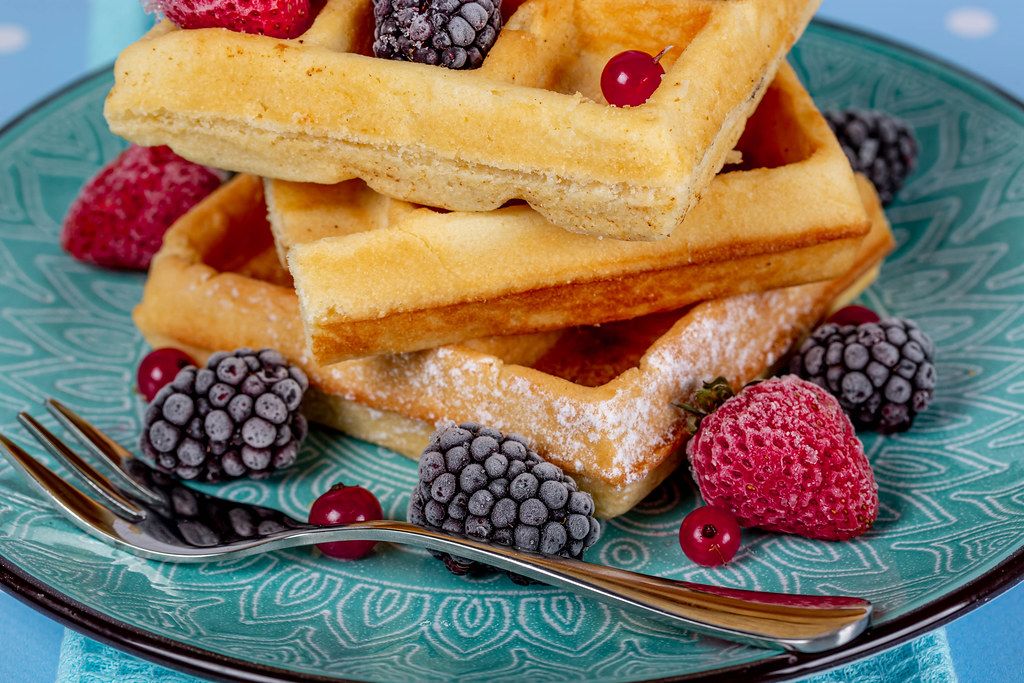 Close-up of Belgian waffles with berries on a blue plate with a fork