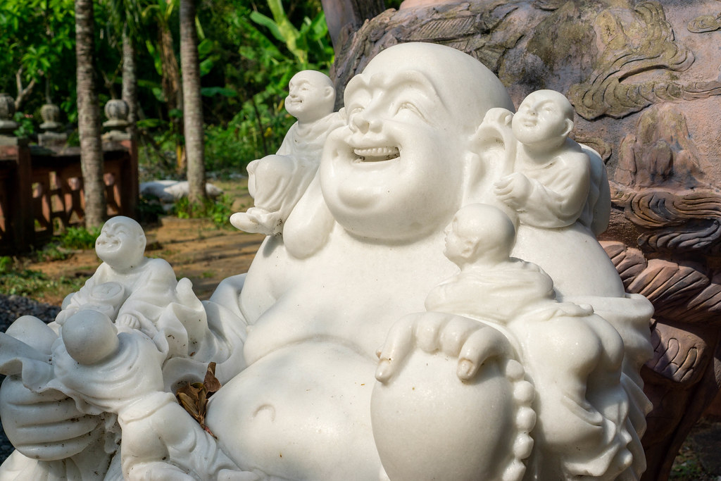 Close Up of White Laughing Buddha with Five Happy Children Marble Statue in a Garden in front of Tam Thai Pagoda at Marble Mountains in Da Nang, Vietnam