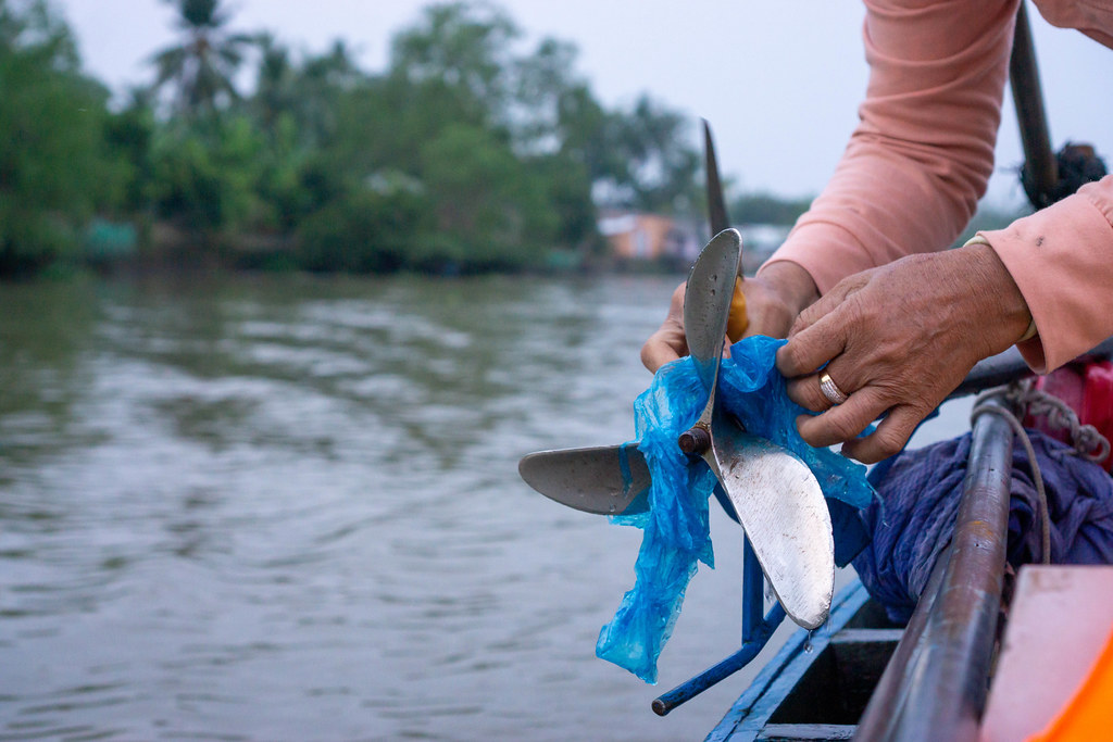Close Up Photo of a Woman removing a Plastic Bag stuck in a Boat Propeller with a Knife and her Hands