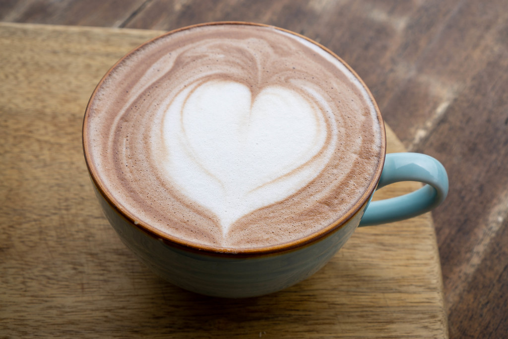Close Up Photo of Hot Cappuccino Coffee in a Ceramic Mug with Latte Art Heart on a Wooden Background
