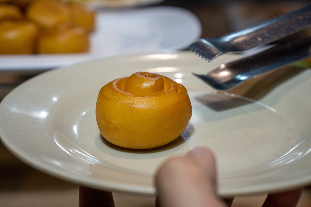 Close Up Photo of Person placing a Deep Fried Mantou Bun with Tongs on a Ceramic Plate at a Buffet in a Restaurant