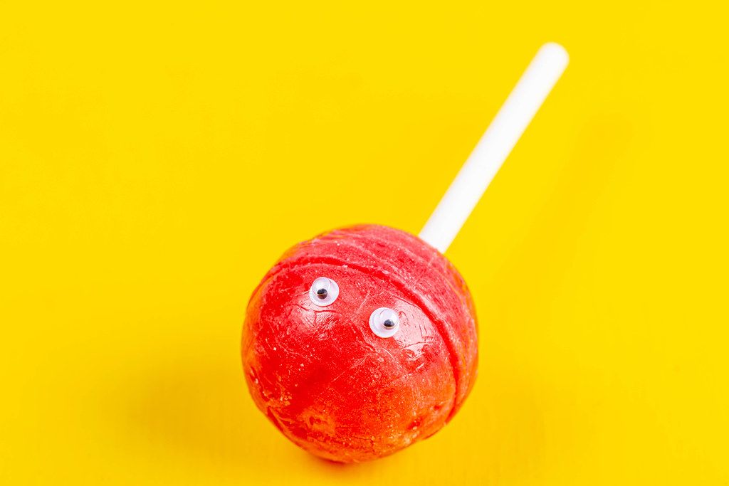 Close-up red lollipop with eyes on a yellow background