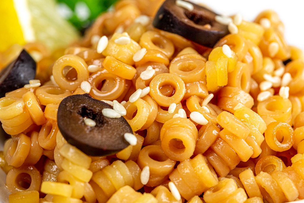 Close-up, round cooked macaroni with black olives and sesame seeds