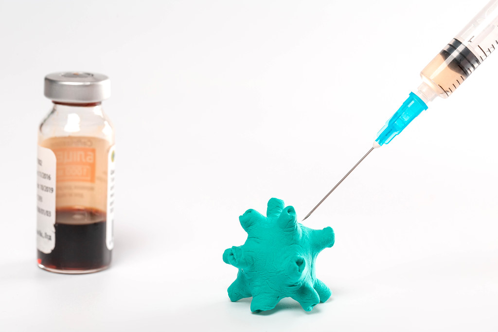 Close-up syringe with vaccine and virus on white background