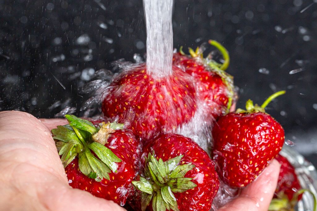 Close up, the hand with the strawberries under running tap water