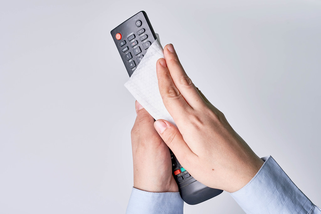 Close-up view of hand using antibacterial wet wipe for disinfecting home TV remote control