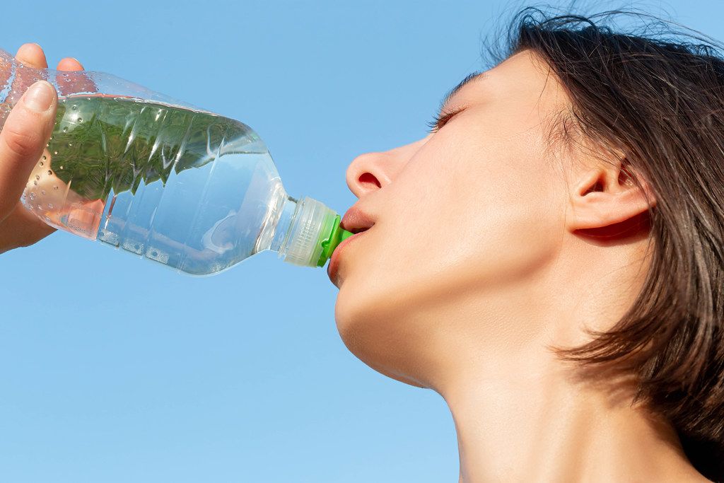 Close up, young attractive woman drinking water on sky background