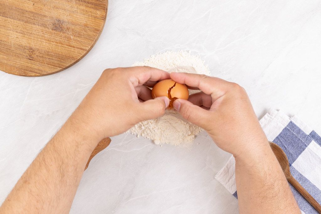 Closeup photo of baker Cracking Egg for dough