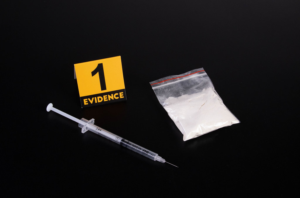 Cocaine and syringe with evidence marker on dark background