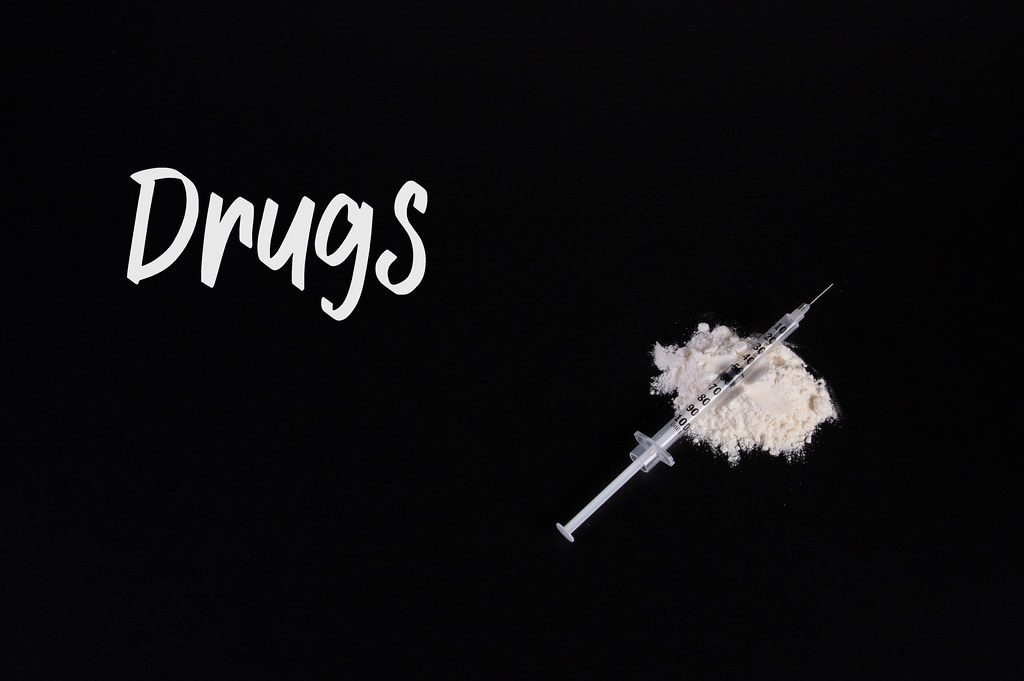 Cocaine powder with syringe and Drugs text on black table