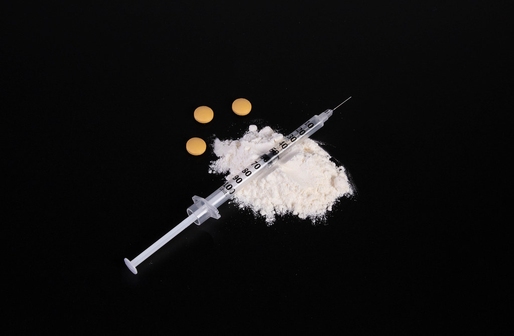 Cocaine powder with syringe and pills on black table