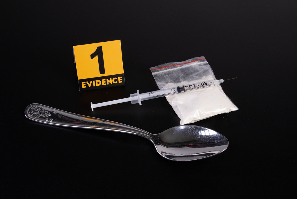 Cocaine, syringe and spoon with evidence marker on dark background