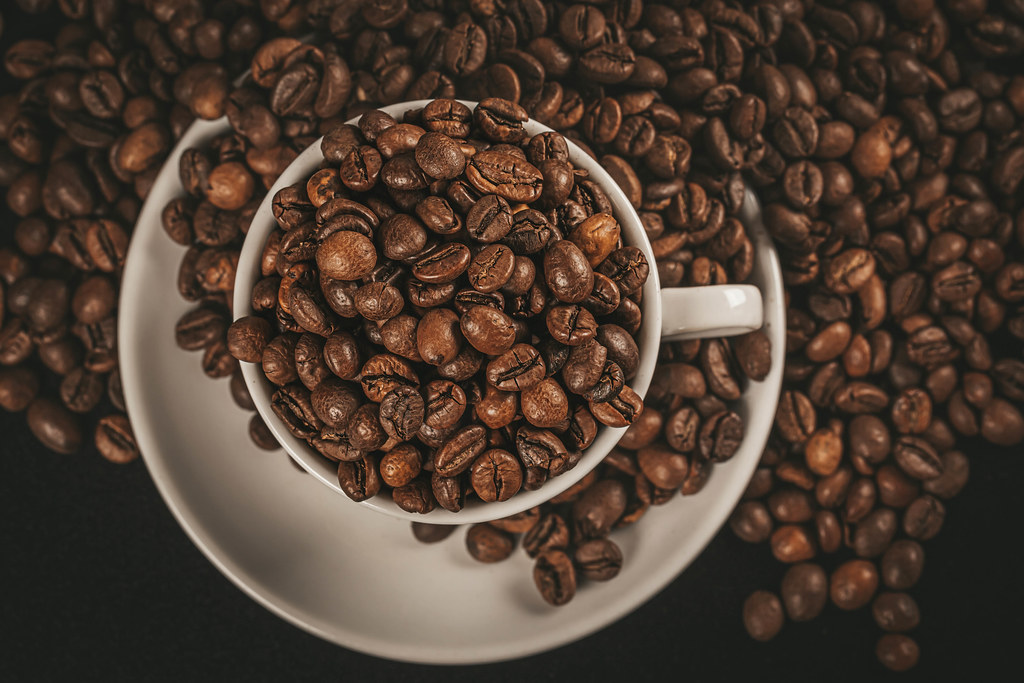 Coffee background, roasted coffee beans in a white cup, top view