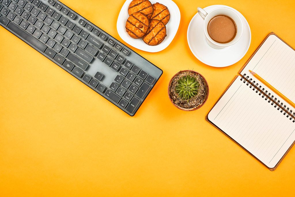 Coffee break. Pc keyboard, notepad, coffee cup and sweet cookies on yellow