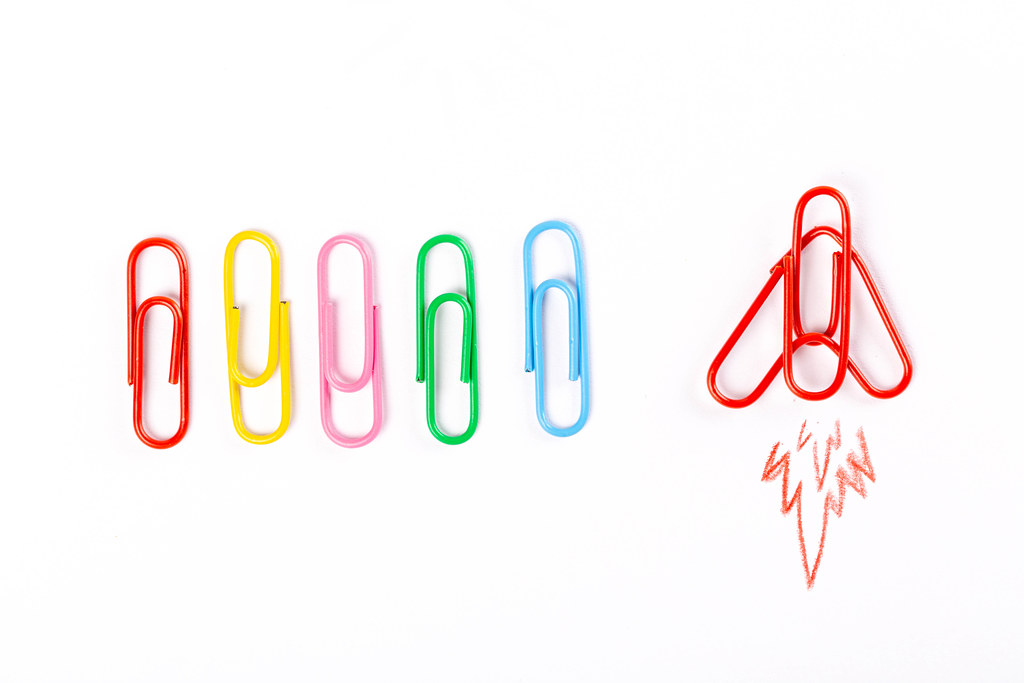 Colored paper clips on white background and airplane take off, forward movement concept