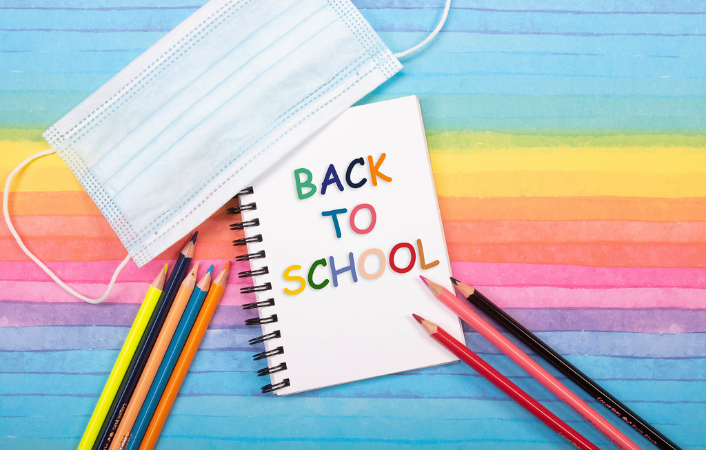 Colored pencils, medical face mask and notebook with back to School text on colorful background