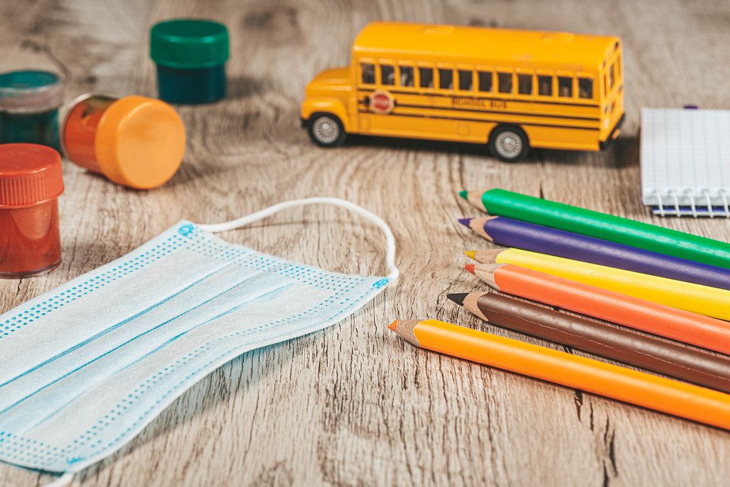 Colored pencils, paints, mask and school bus on wooden background