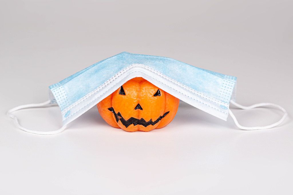 Concept Halloween , COVID-19 prevention. Pumpkin candle with medical mask