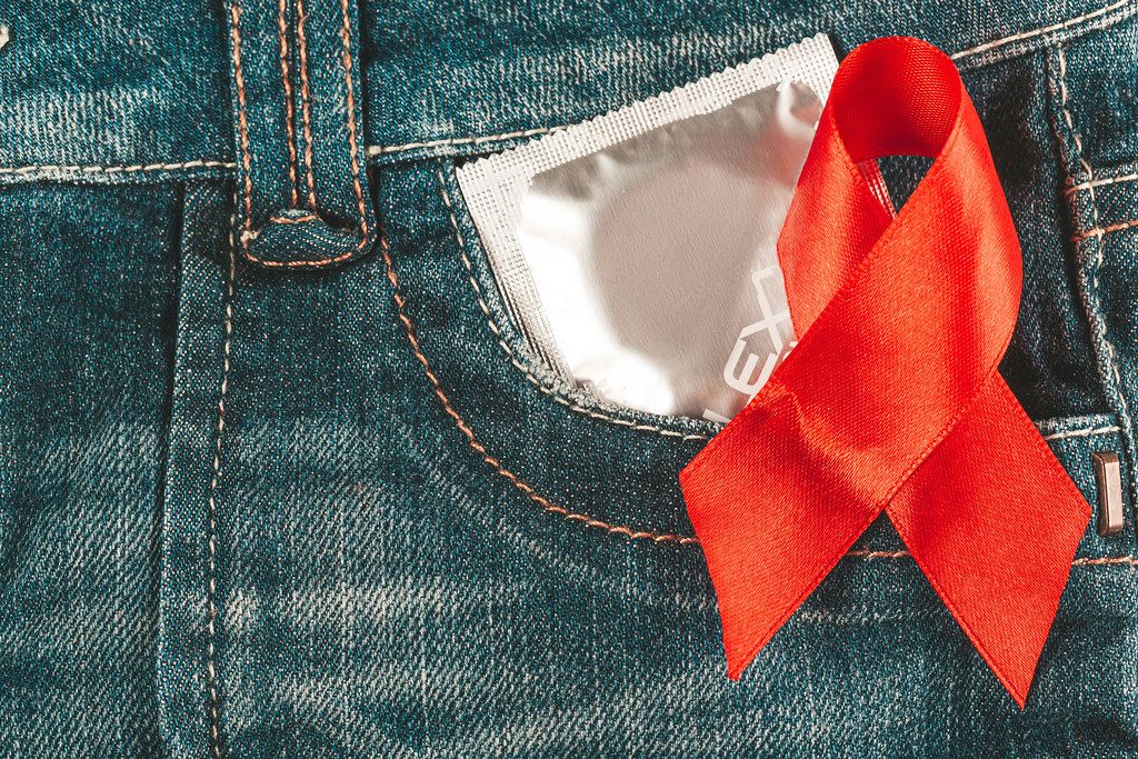 Condom in jeans pocket with red awareness ribbon for aids and hiv, close up