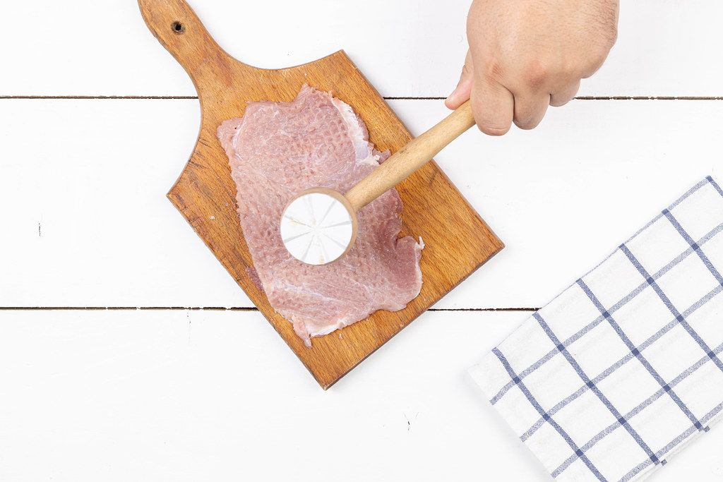 Cook beats Pork Raw Meat with wooden hammer