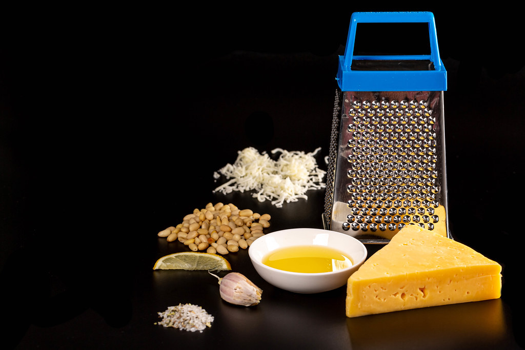 Cooking concept-grater, cheese, pine nuts and spices on a black background