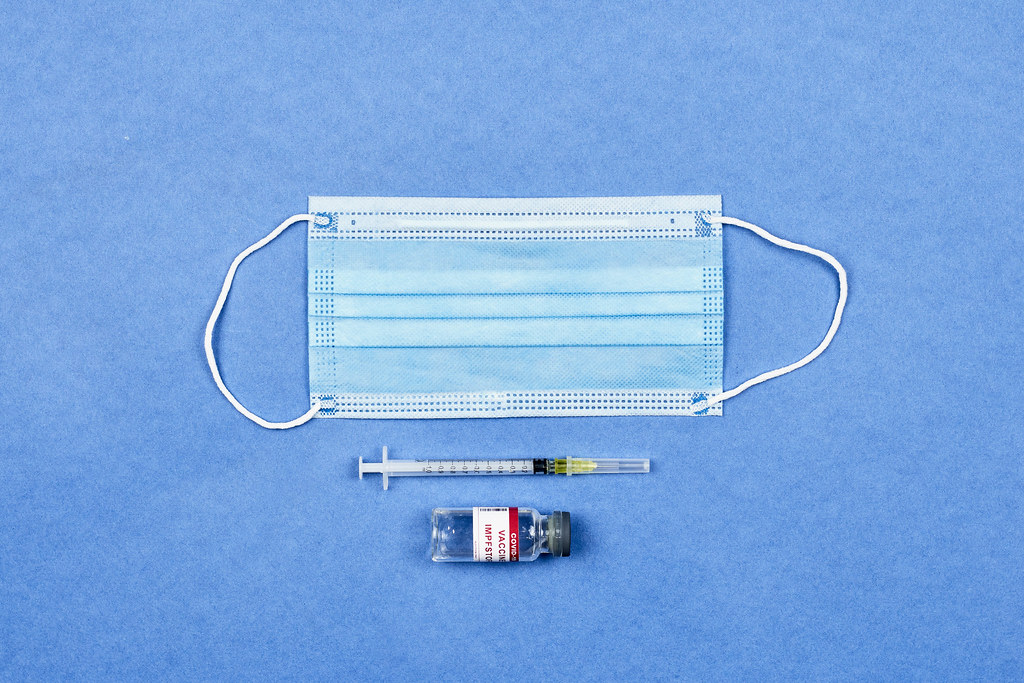 Coronavirus vaccine with syringe and face mask on blue