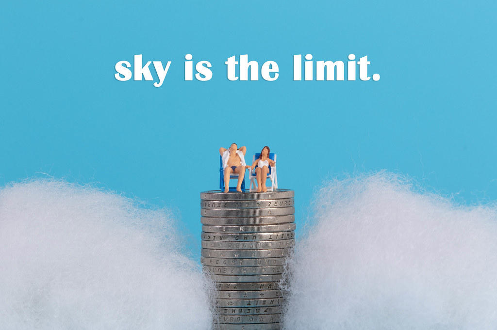 Couple sitting on top of a coinstack surrounded with clouds and Sky is the limit text