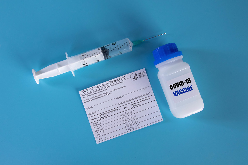 Covid-19 vaccine with syringe and vaccination record card on blue backgroung