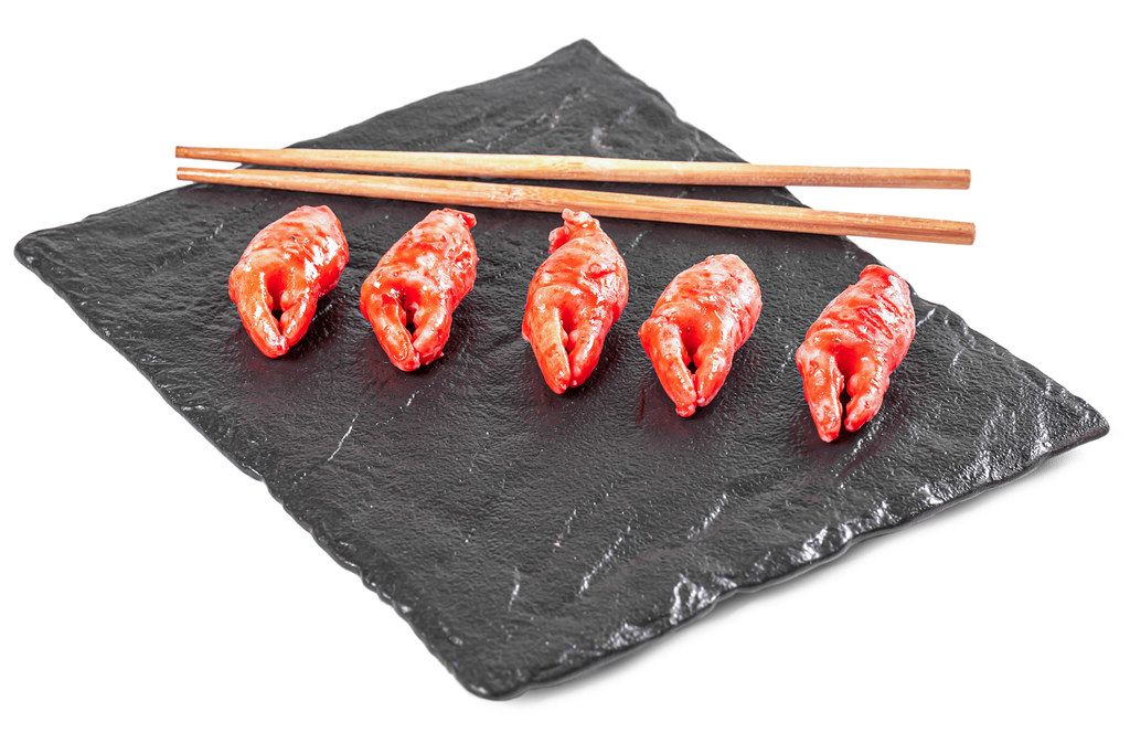 Crab claws marinated in a spicy sauce with herbs on a black stone tray