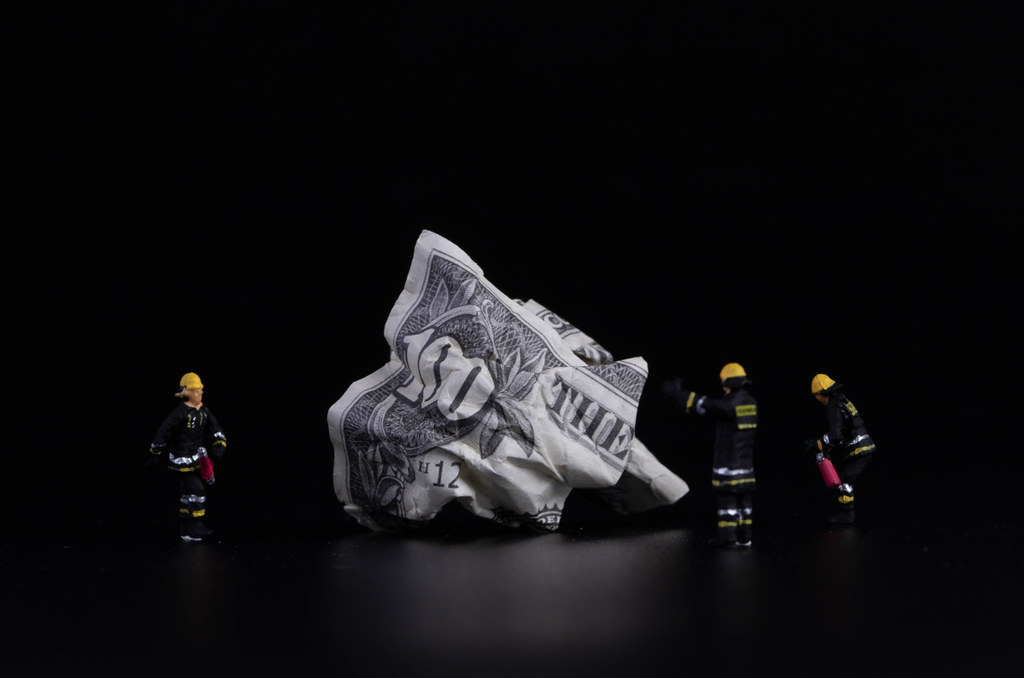 Crushed 100 dollar banknote with miniature firefighters on black background