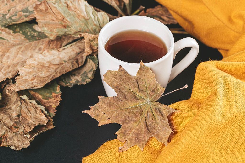 Cup of tea with autumn leaves and yellow scarf