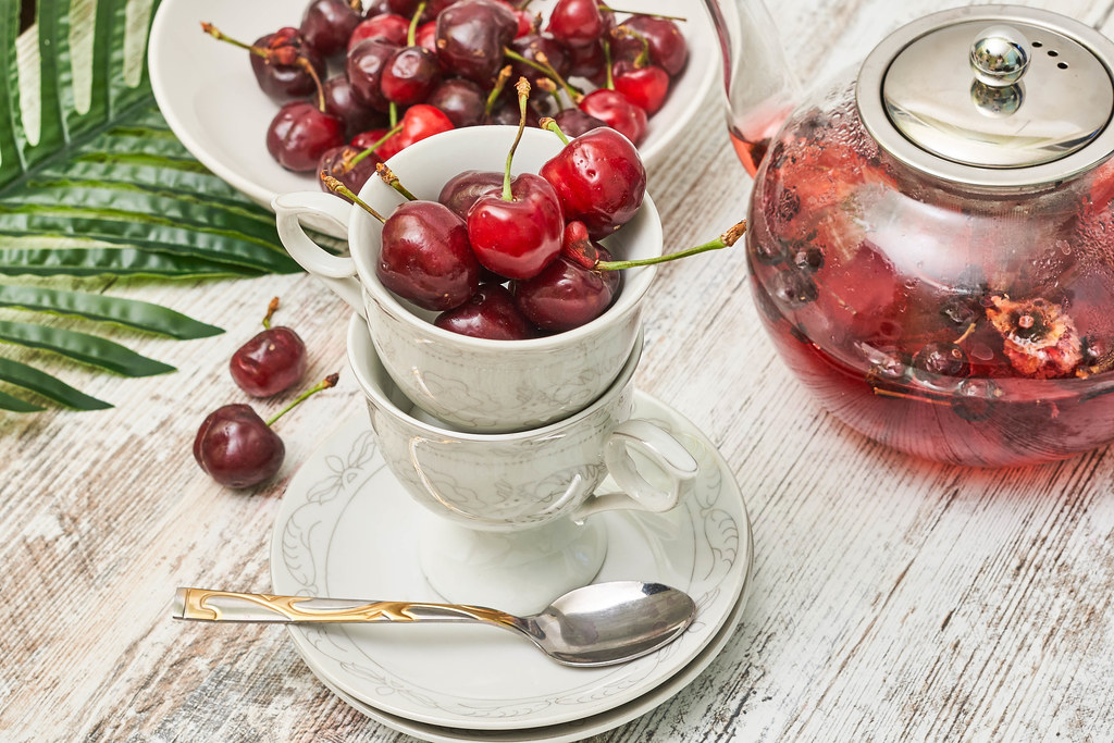Cups full of sweet cherry fruits and teapot with fruit tea
