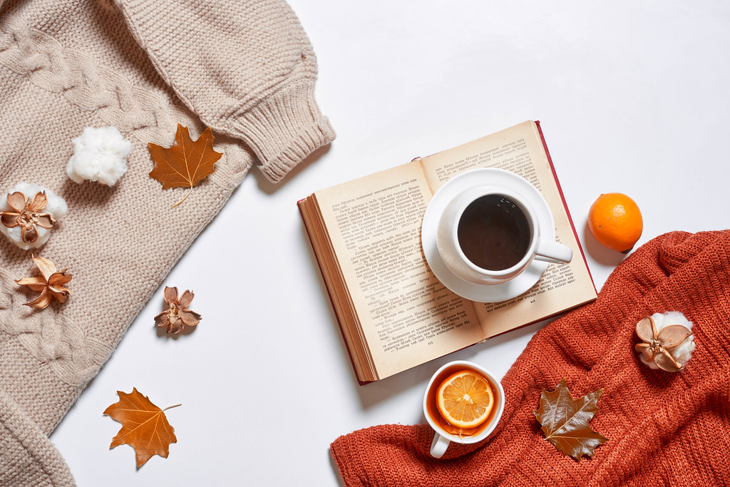 Cups of tea and coffee, cozy knitted sweaters, autumn leaves, open book on white background