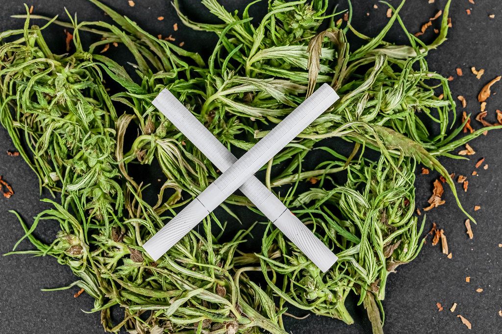 Danger concept, cross made of cigarettes on a heap of cannabis, top view