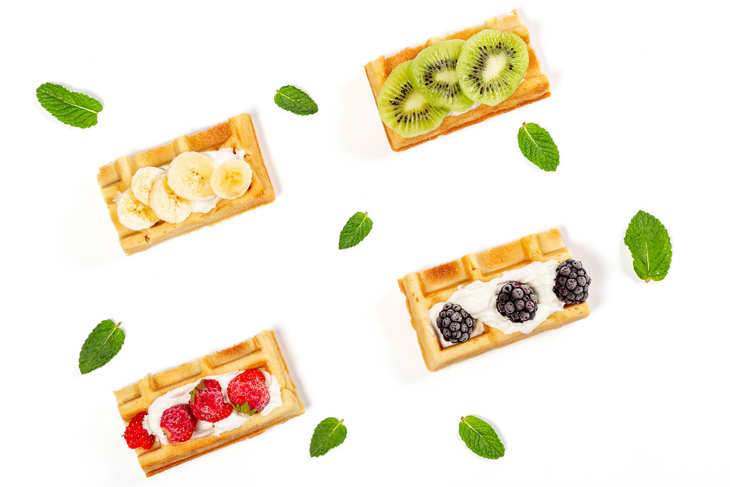 Delicious belgian waffles with pieces of fruits and berries on a white background with mint leaves