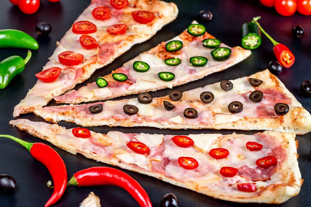 Delicious slices of assorted pizza with spices on a dark background