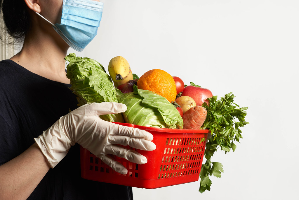 Delivery service worker in face mask and medical gloves brings ordered fresh vegetables