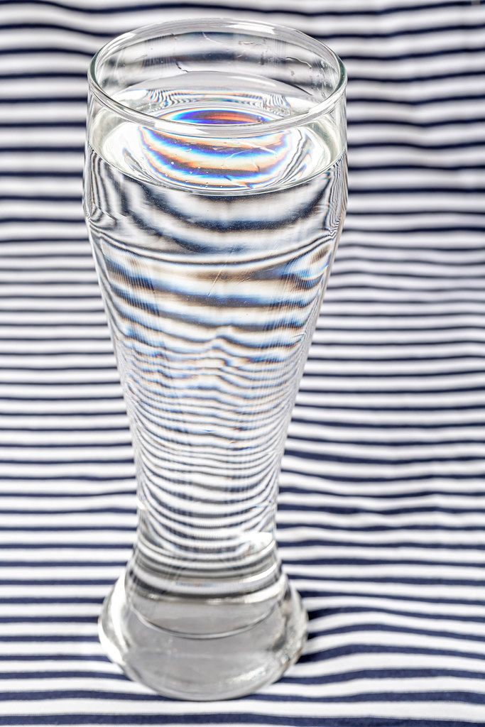 Distortion of white and black striped background with the help water in glass