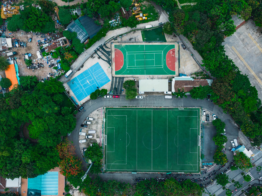 Drohnenaufnahme in der Vogelperspektive von einem Fußballplatz, einem Tennisplatz und einem Basketballplatz mit vielen parkenden Motorrollern in Ho Chi Minh City, Vietnam