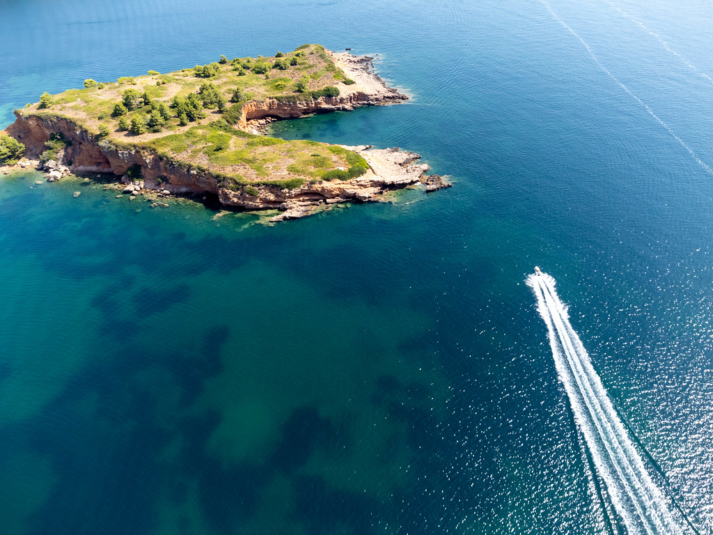 Drone photo: a motorboat skirts the jagged coastline of Kokkinonisi (