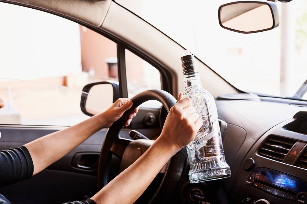 Drunk driving concept - a person driving car with bottle of vodka