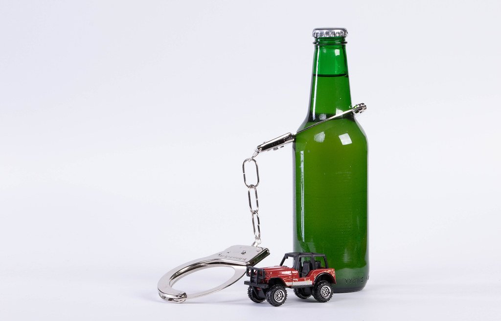 Drunk driving concept. Beer bottle chained with handcuffs with miniature car on white background