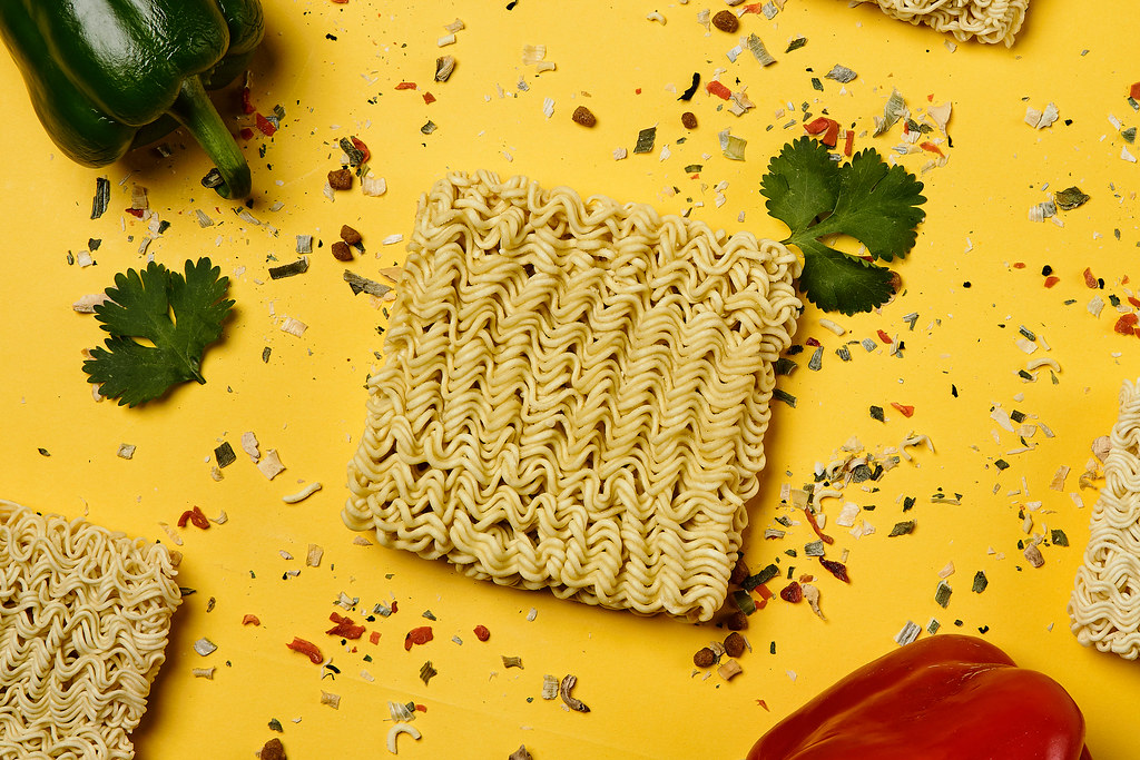 Dry instant noodle block with seasonings on yellow background