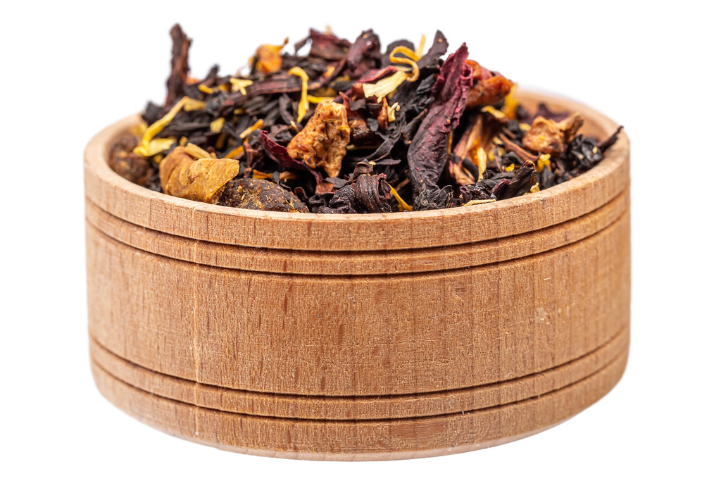 Dry tea with hibiscus and dried fruits in a wooden bowl on a white background