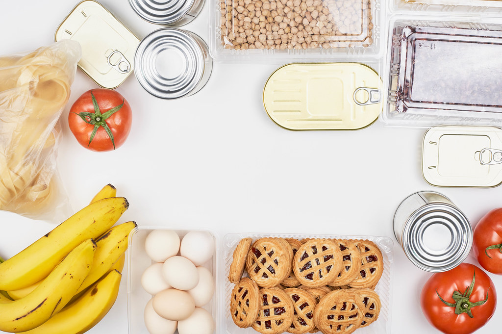 Ein Rahmen aus Lebensmitteln mit Platz für Text in der Mitte: Eier, Bananen, Kekse, Blechdosen, Nudeln