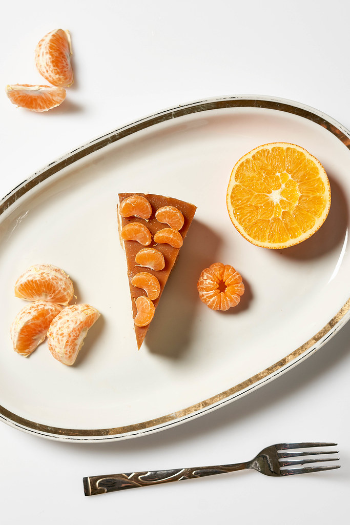 Ein Stück Käsekuchen mit Mandarinenstücken obendrauf, serviert mit Zitrusfrüchten