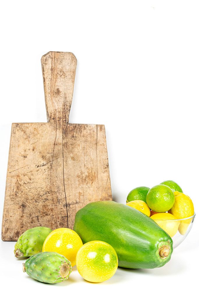 Exotic fruit on a white background with old kitchen board. Yellow passion fruit, papaya, cactus fruit, limes and lemons
